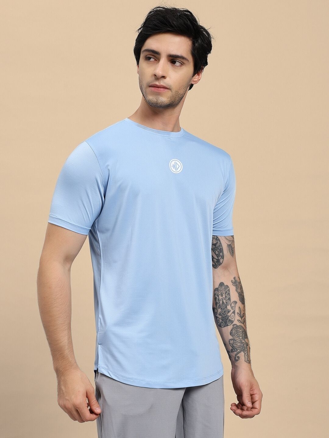 Man wearing a light blue t-shirt with a logo on a beige background