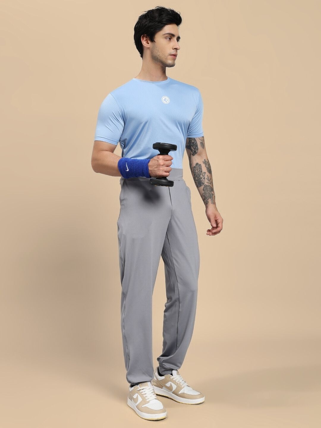 Man holding a dumbbell wearing a blue shirt and gray pants on a beige background