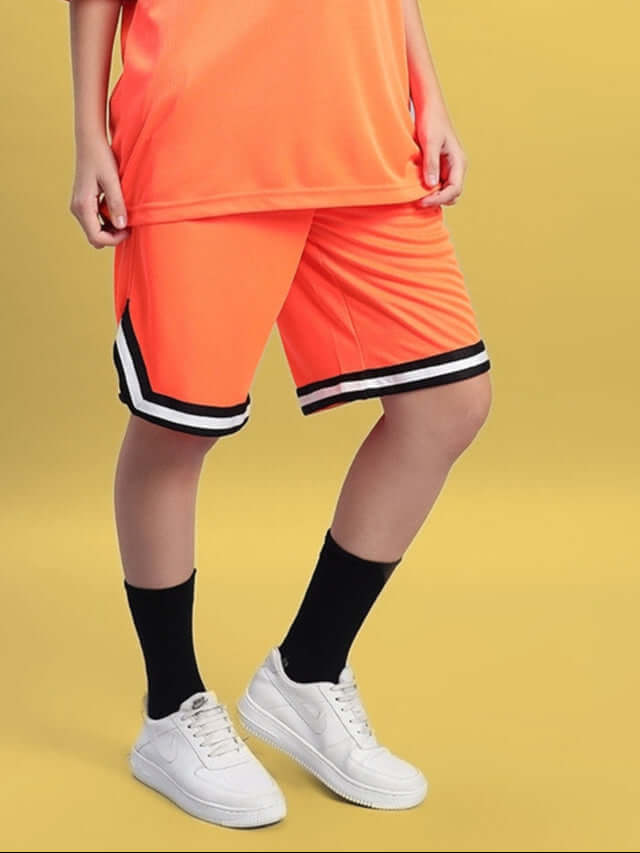 Woman wearing orange regular fit shorts with black stripes, paired with a matching top and white sneakers.