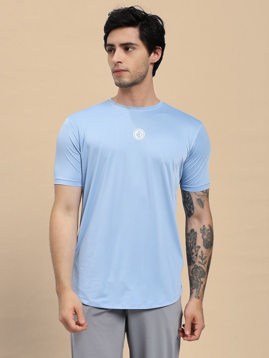 Man wearing a light blue t-shirt with a logo on a beige background