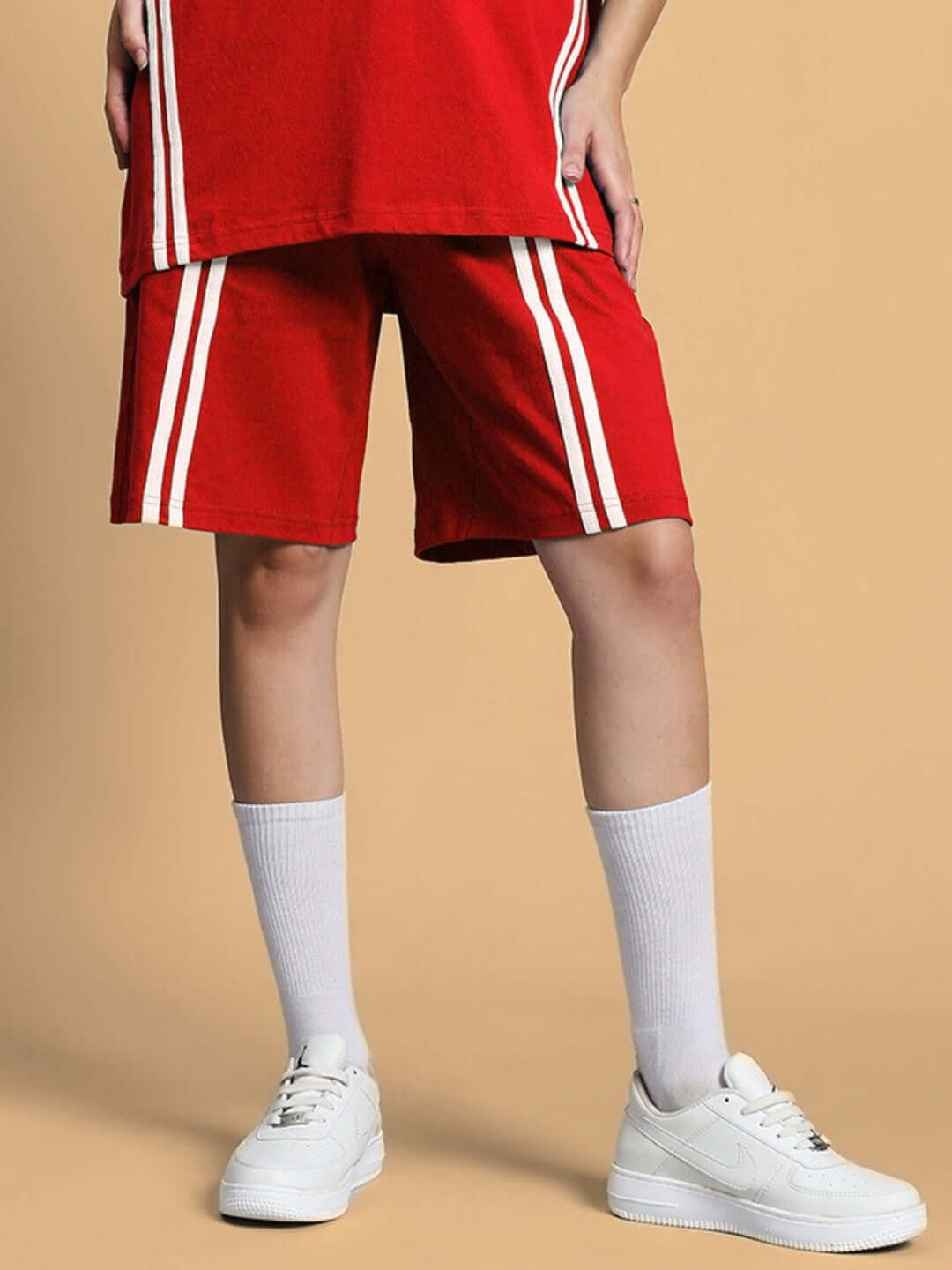 Woman modeling red regular fit shorts with white stripes, suitable for custom fit, shown with white sneakers and socks, perfect for casual wear.
