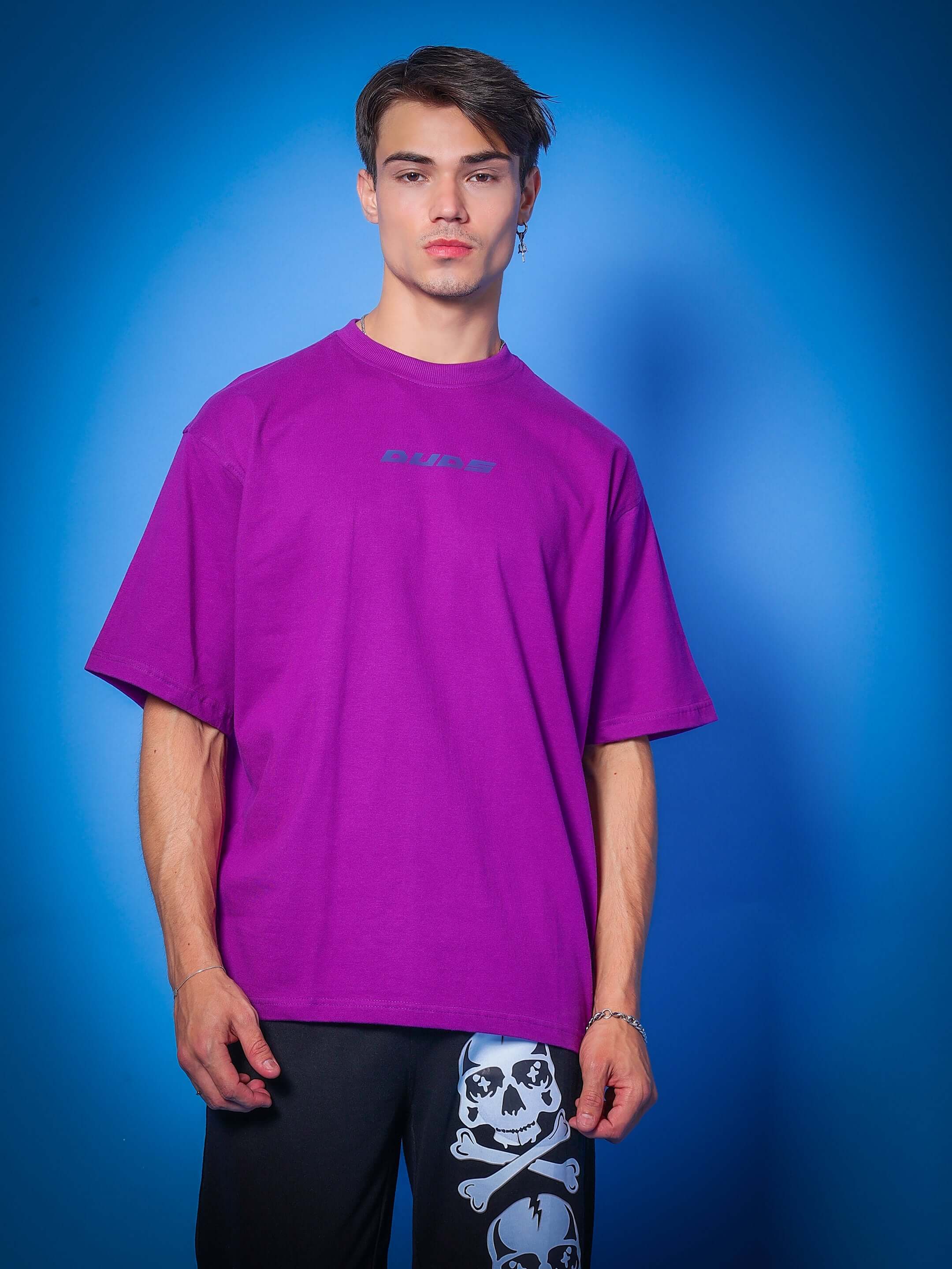 INTERTWINED SNAKE REFLECTOR OVER-SIZED T-SHIRT PURPLE on a model with skull pants, blue background