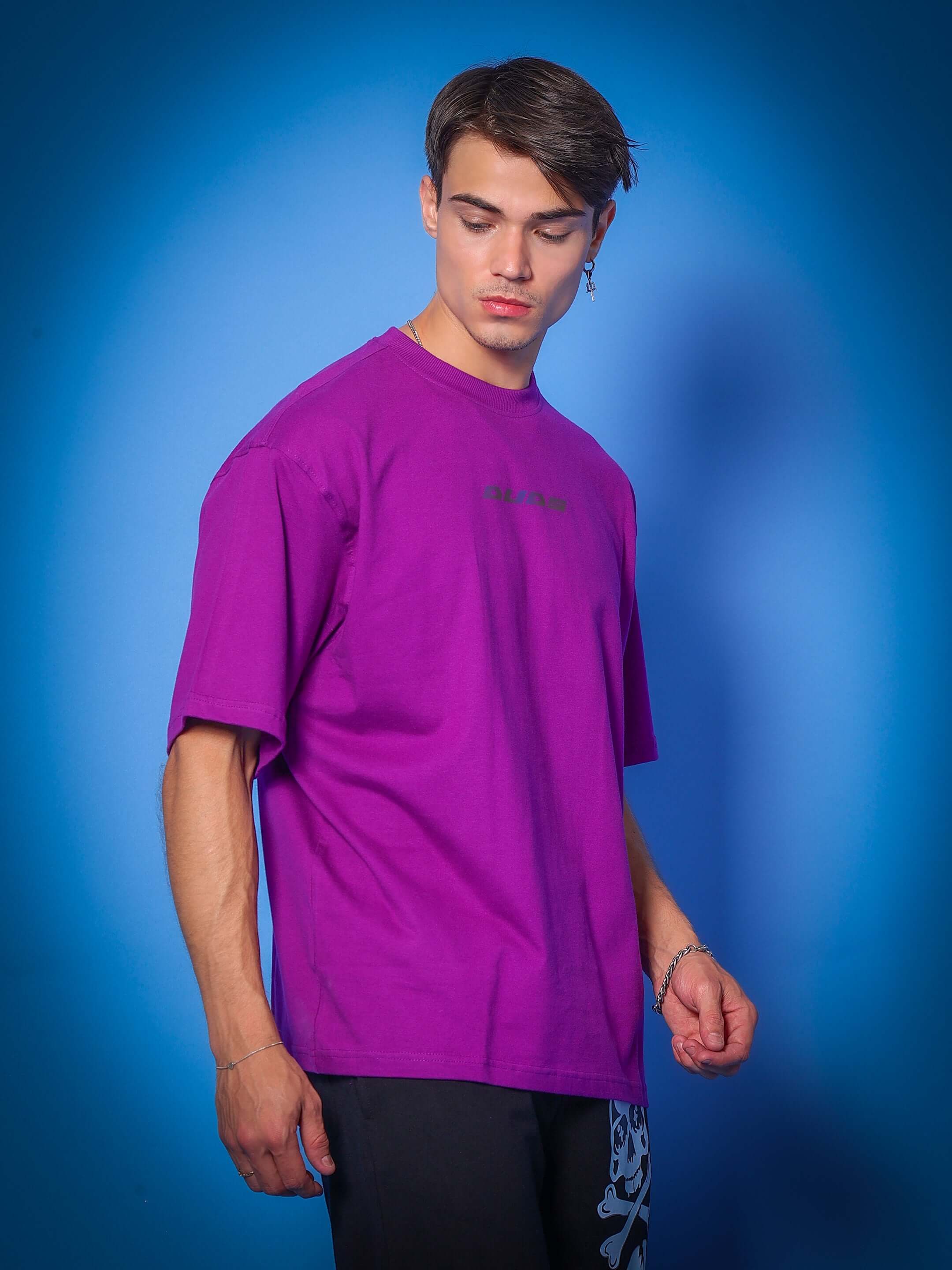 Model wearing INTERTWINED SNAKE REFLECTOR OVER-SIZED T-SHIRT PURPLE in front of blue background