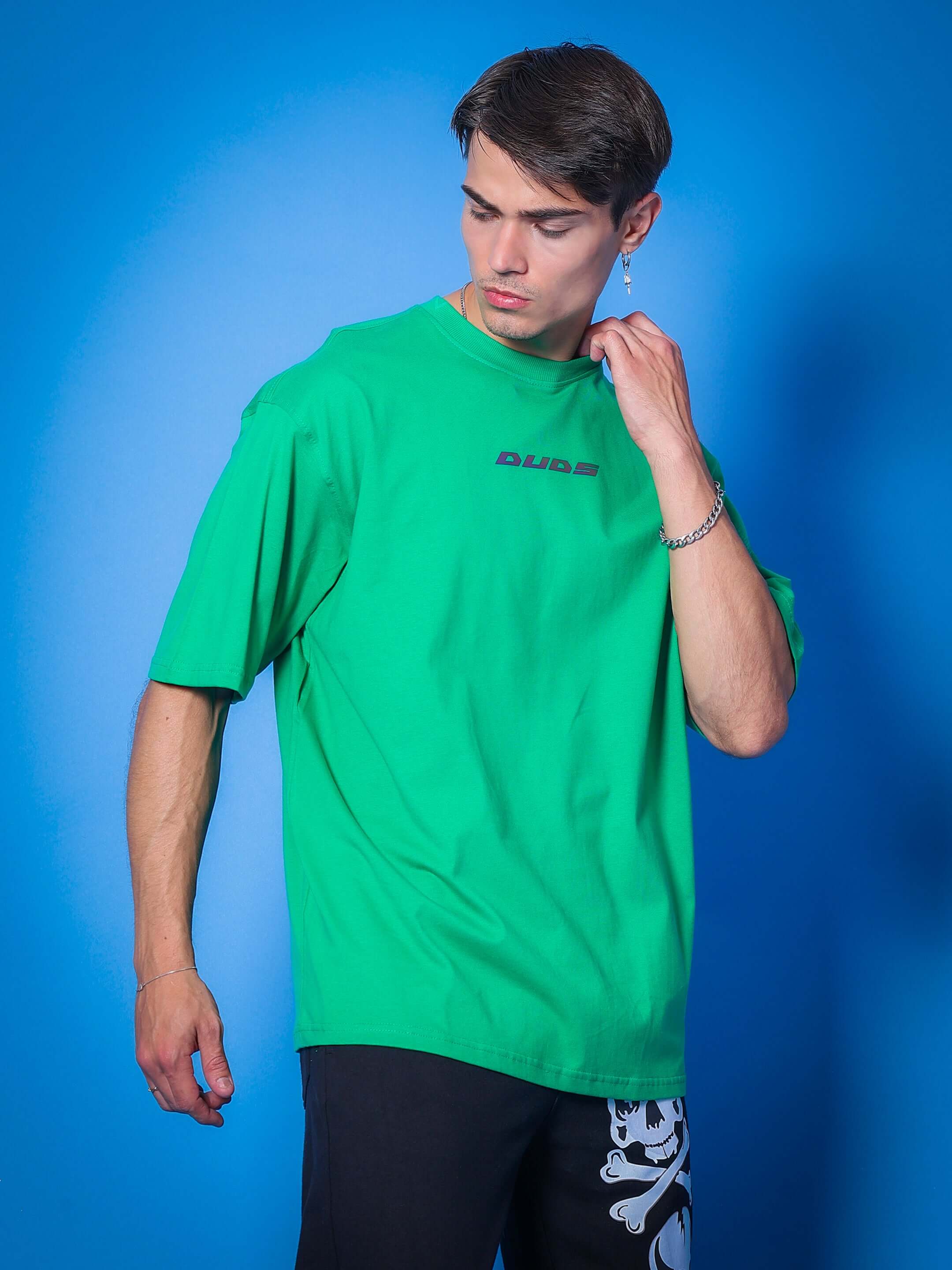 Model wearing MEDUSA GAZE REFLECTOR EYE OVER-SIZED T-SHIRT GREEN against blue background