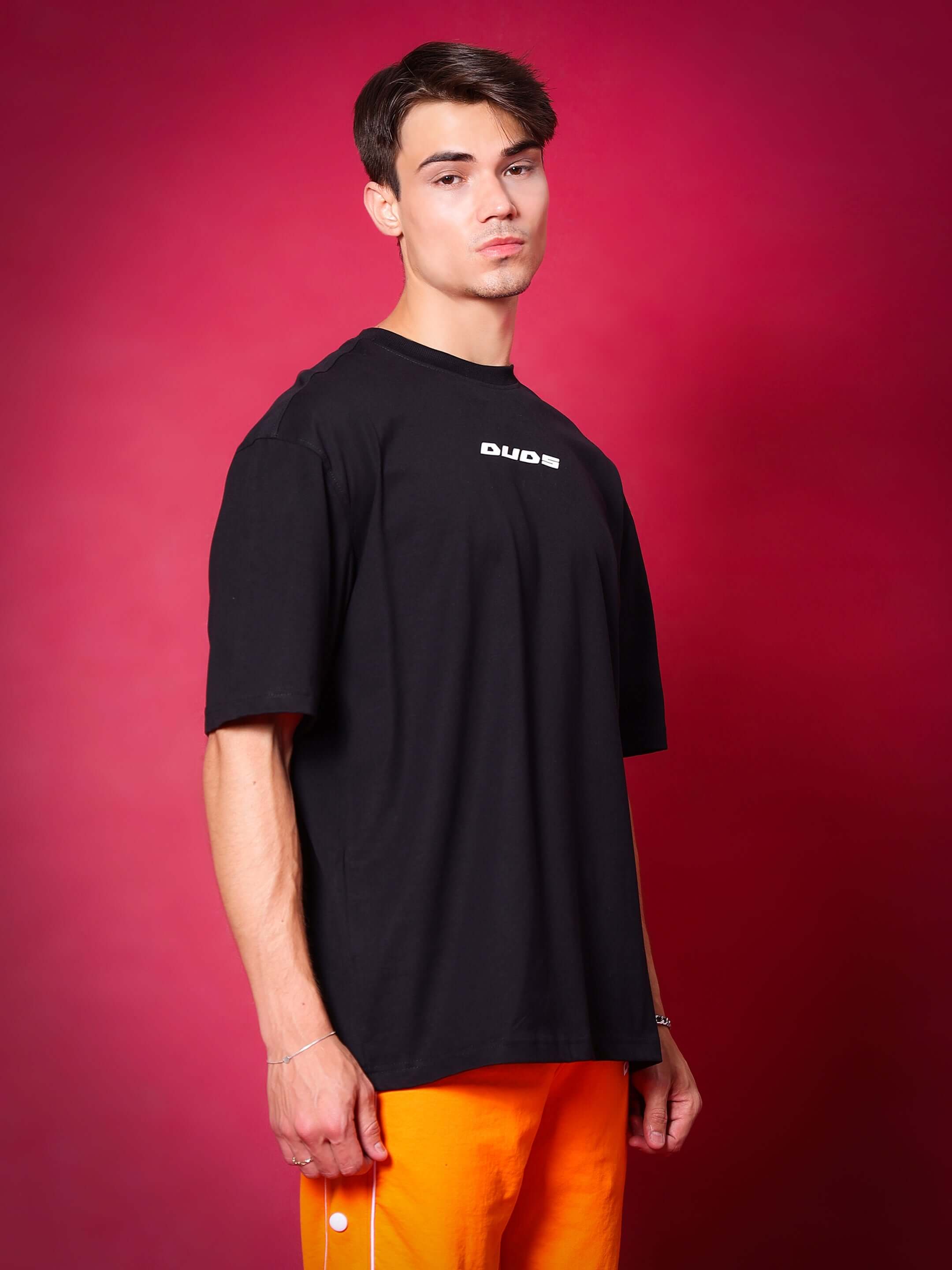 Model wearing GLITTERED HD MOON OVER-SIZED T-SHIRT BLACK by WEAR DUDS against a red background, showcasing streetwear fashion.