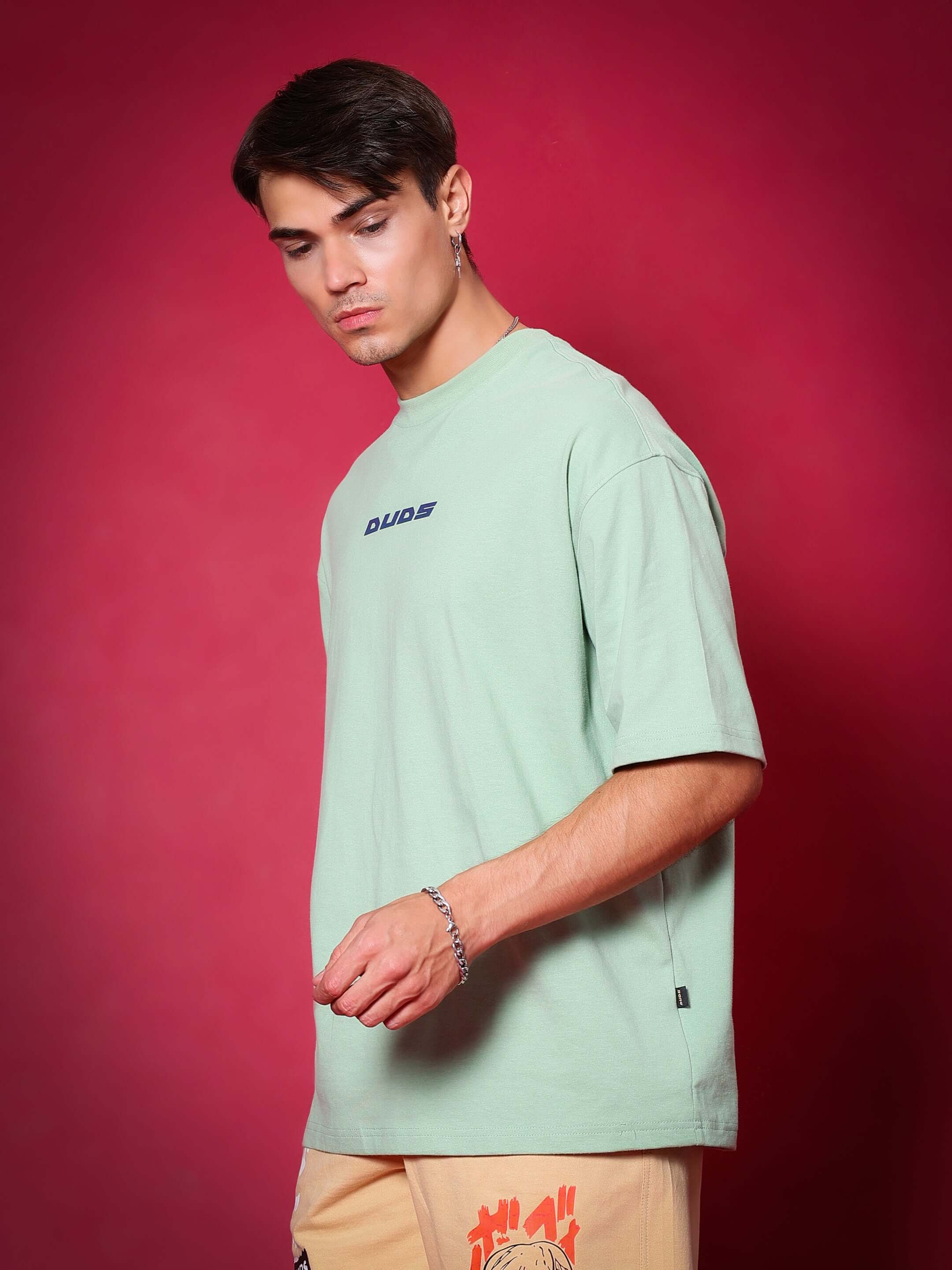 Man wearing a PRAY OVER-SIZED T-SHIRT NYANZA GREEN made of premium cotton French terry, styled with a red background.
