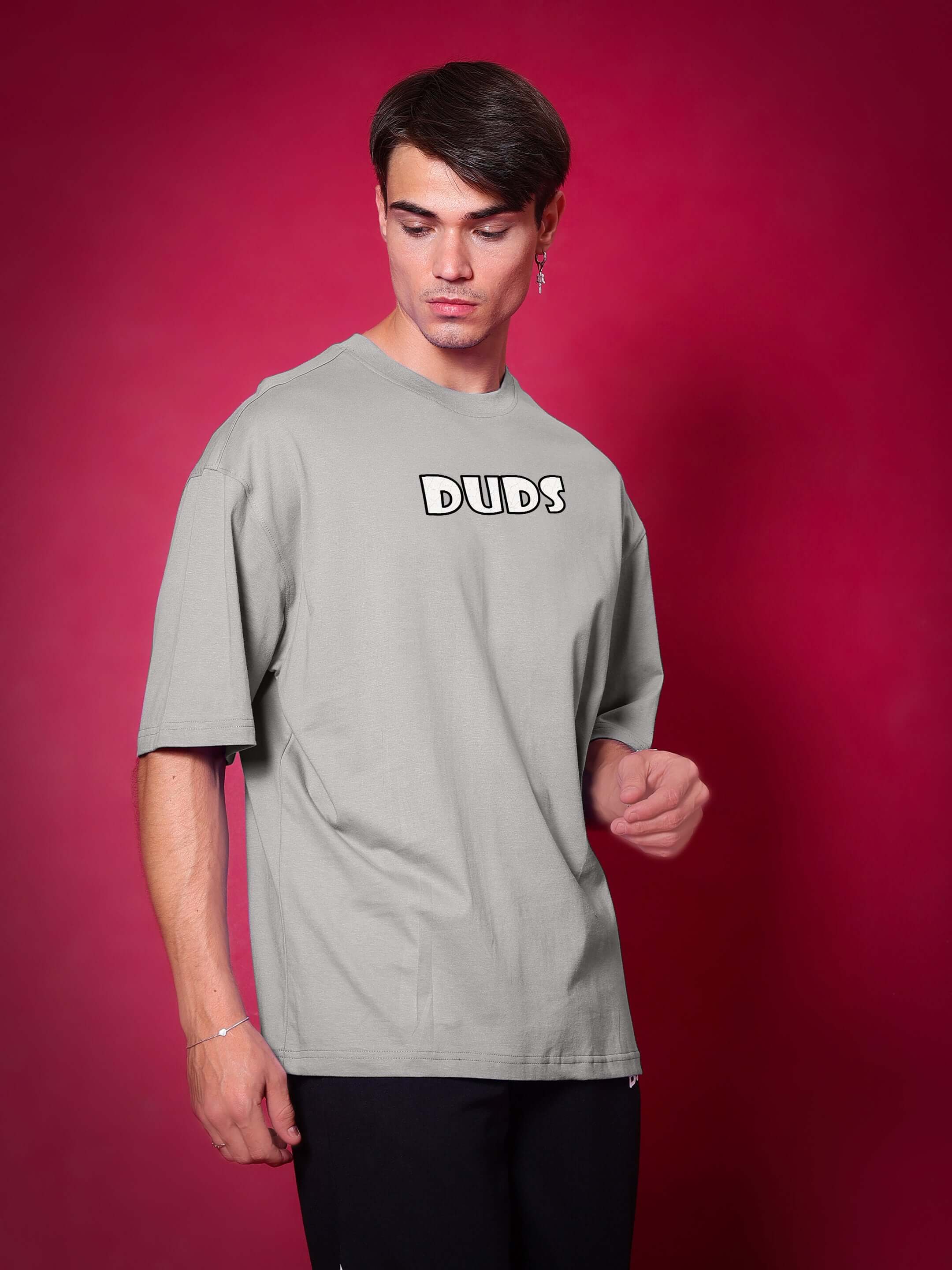 Person wearing WOLF PACK OVER-SIZED T-SHIRT GREY against a red background, showcasing comfortable streetwear look.