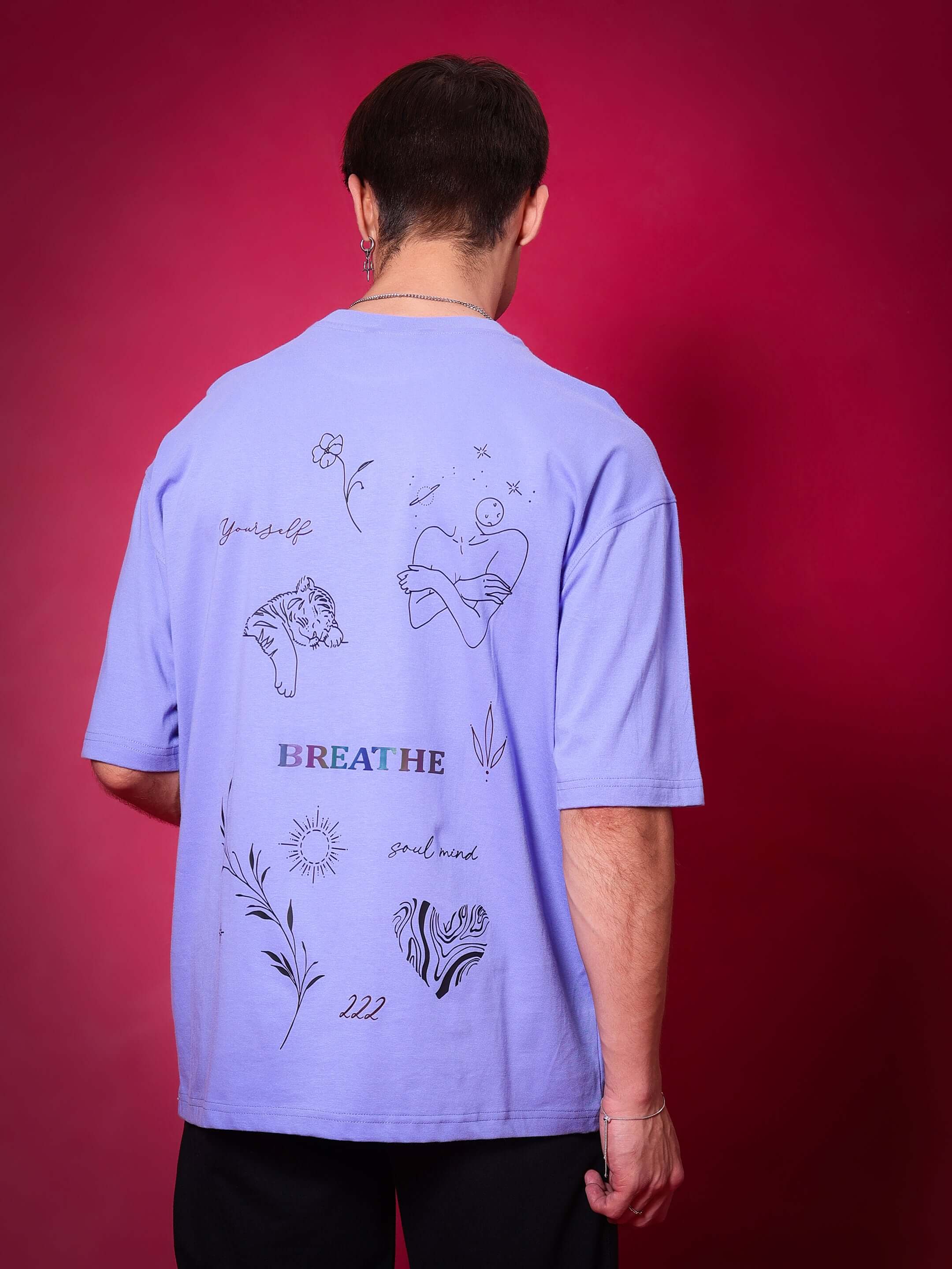Alt Tag: Person wearing BREATHE OVER-SIZED T-SHIRT PERIWINKLE with artistic graphics on back, standing against red background.