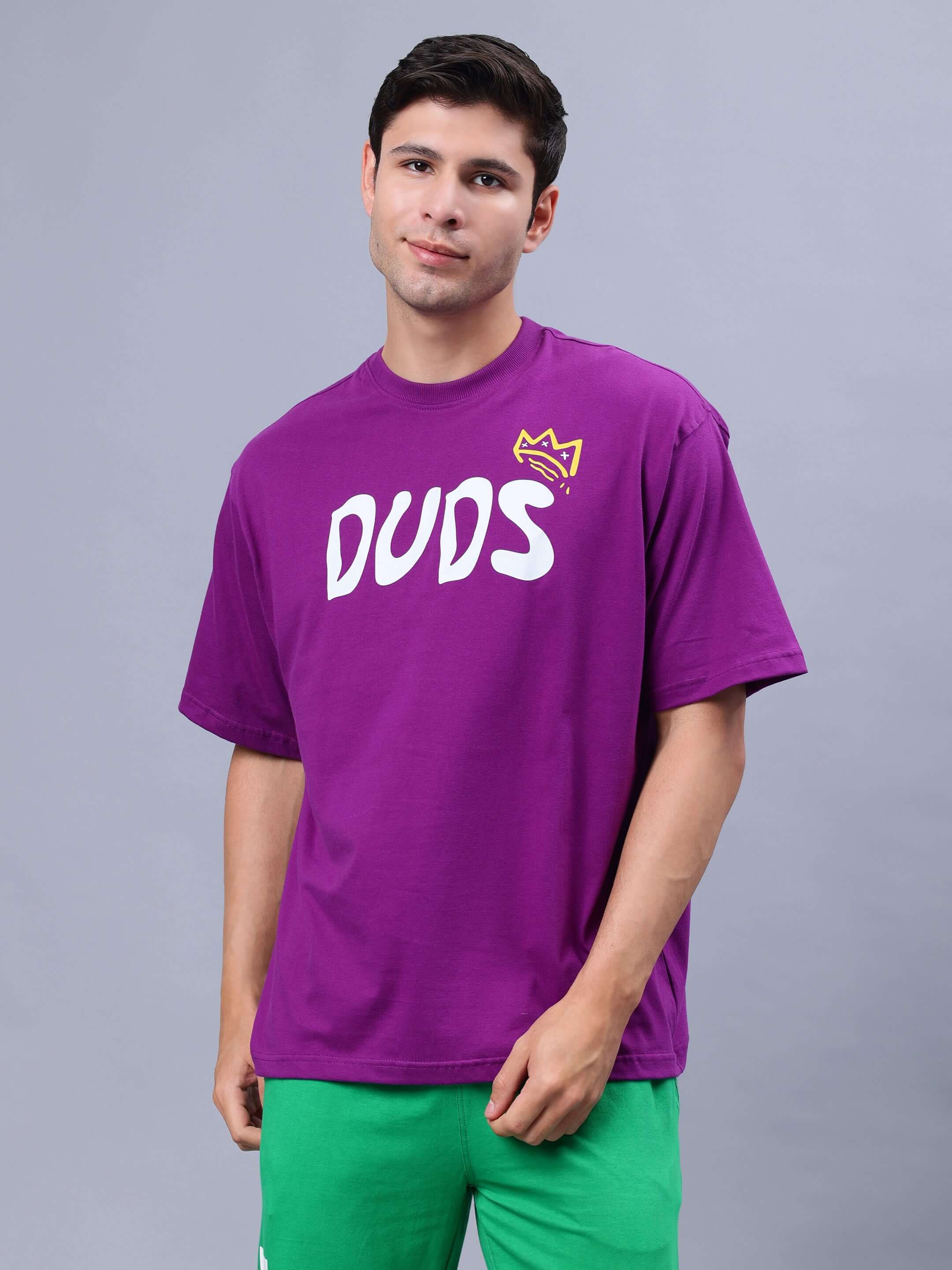 Man wearing MAKE MONEY NOT FRIENDS OVER-SIZED T-SHIRT PURPLE with graphic design and green pants.