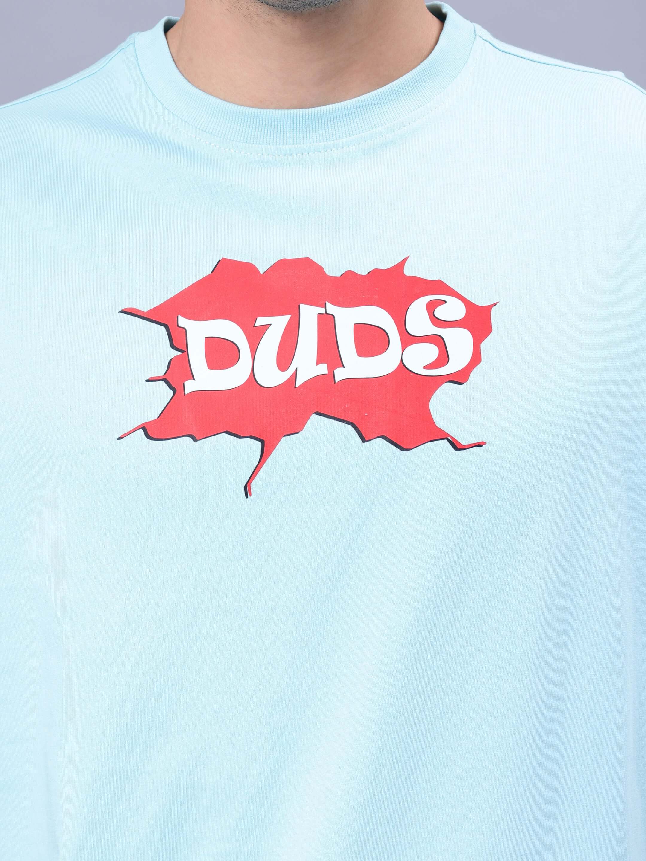 Person wearing RADIO OVER-SIZED T-SHIRT SKY BLUE featuring red DUDS logo.