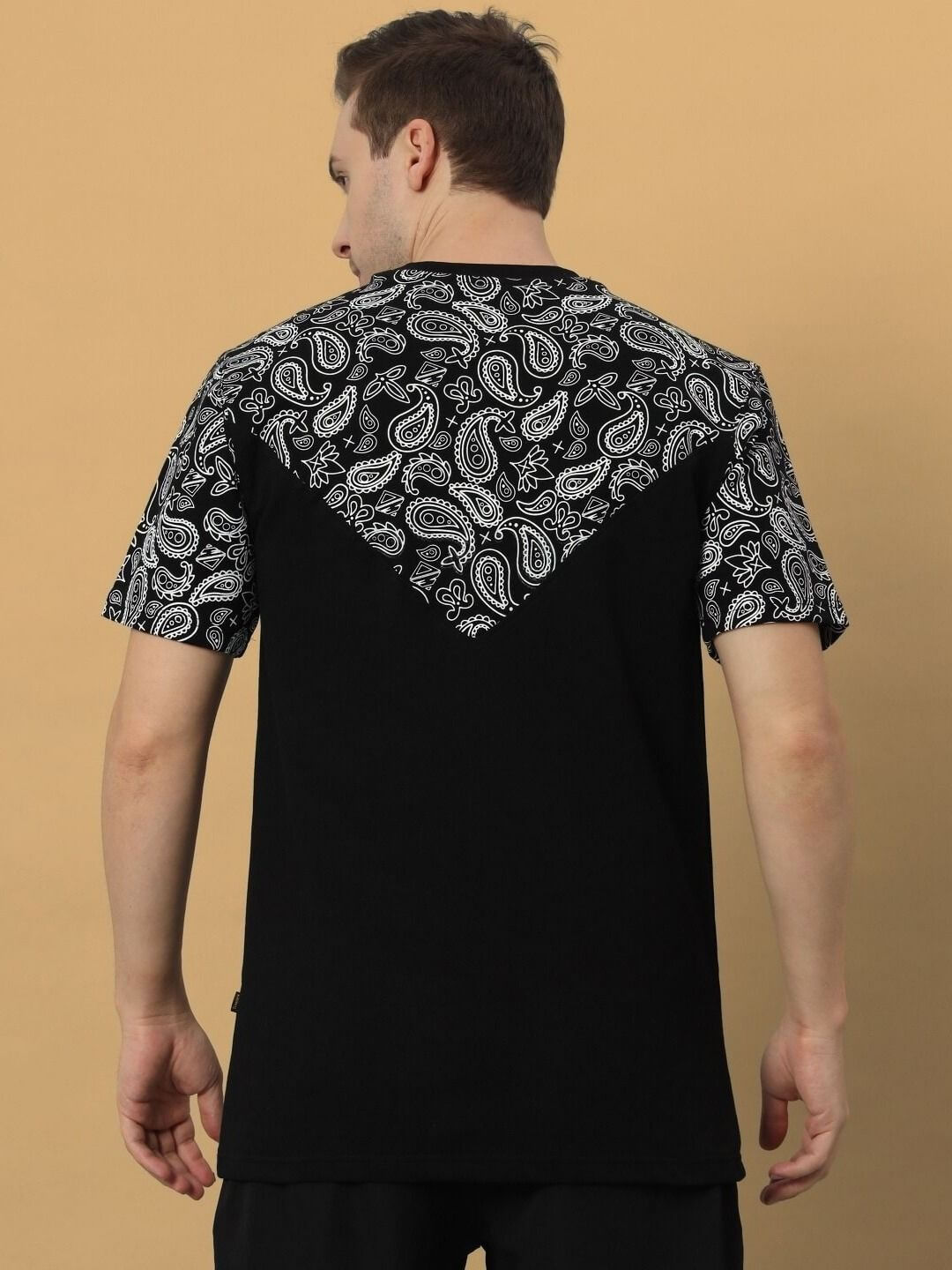 Back view of a man wearing a Balladeer oversized T-shirt in black with paisley pattern accents on shoulders and upper back.