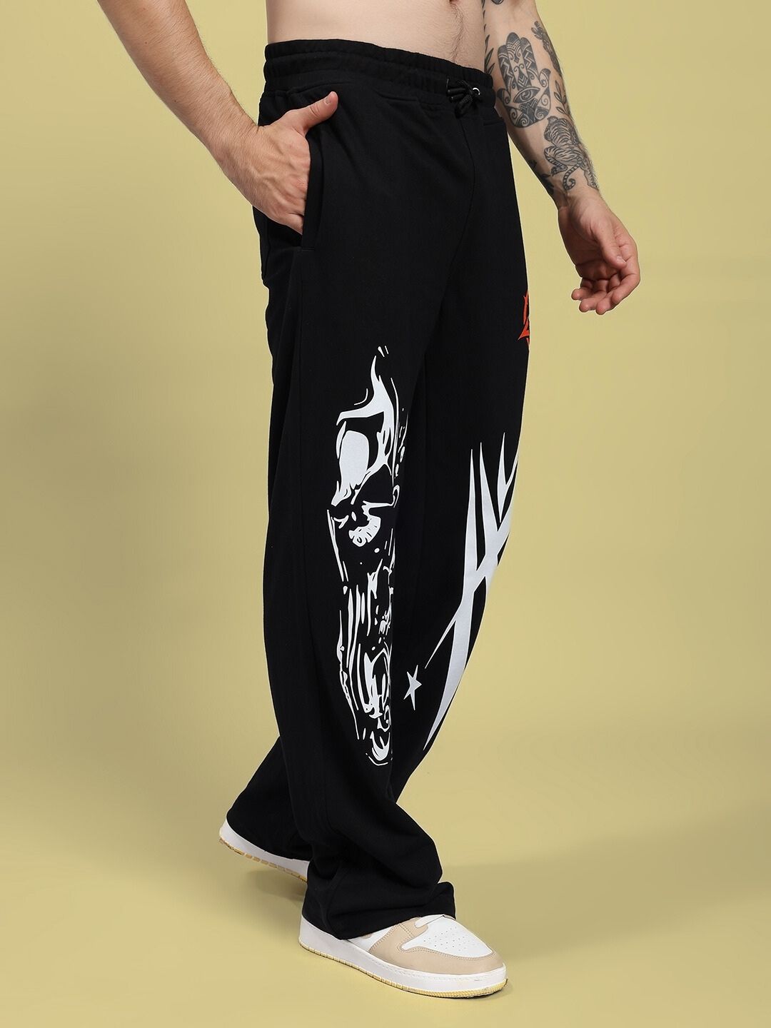 Black sweatpants with white graphic design worn by a person on a beige background
