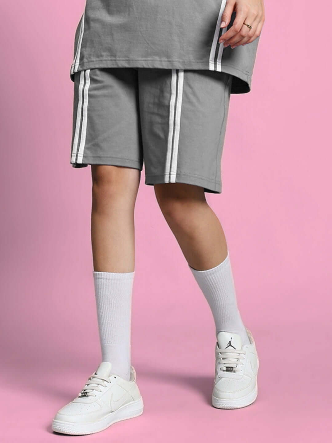 Grey women's regular fit shorts modeled with white sneakers and socks on a pink background.