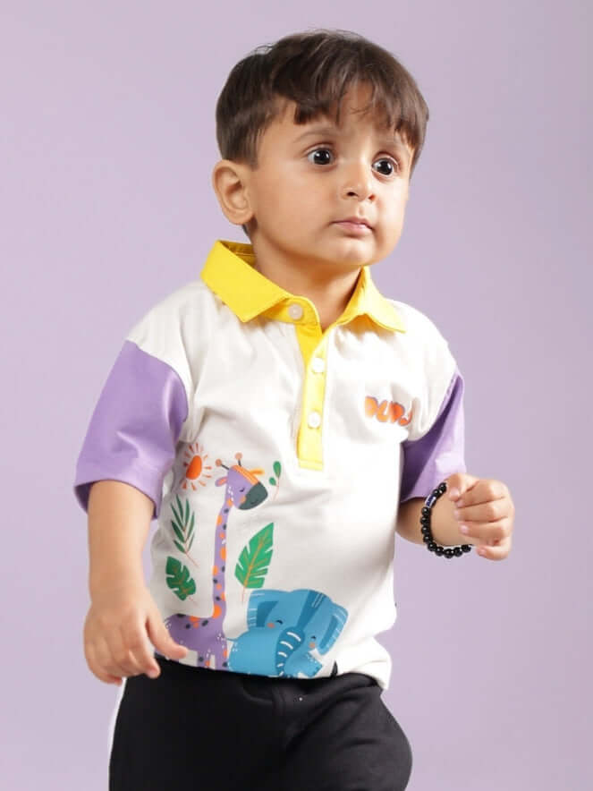 Toddler wearing a colorful short-sleeve shirt with animal patterns, featuring purple and yellow accents, standing against a plain background.