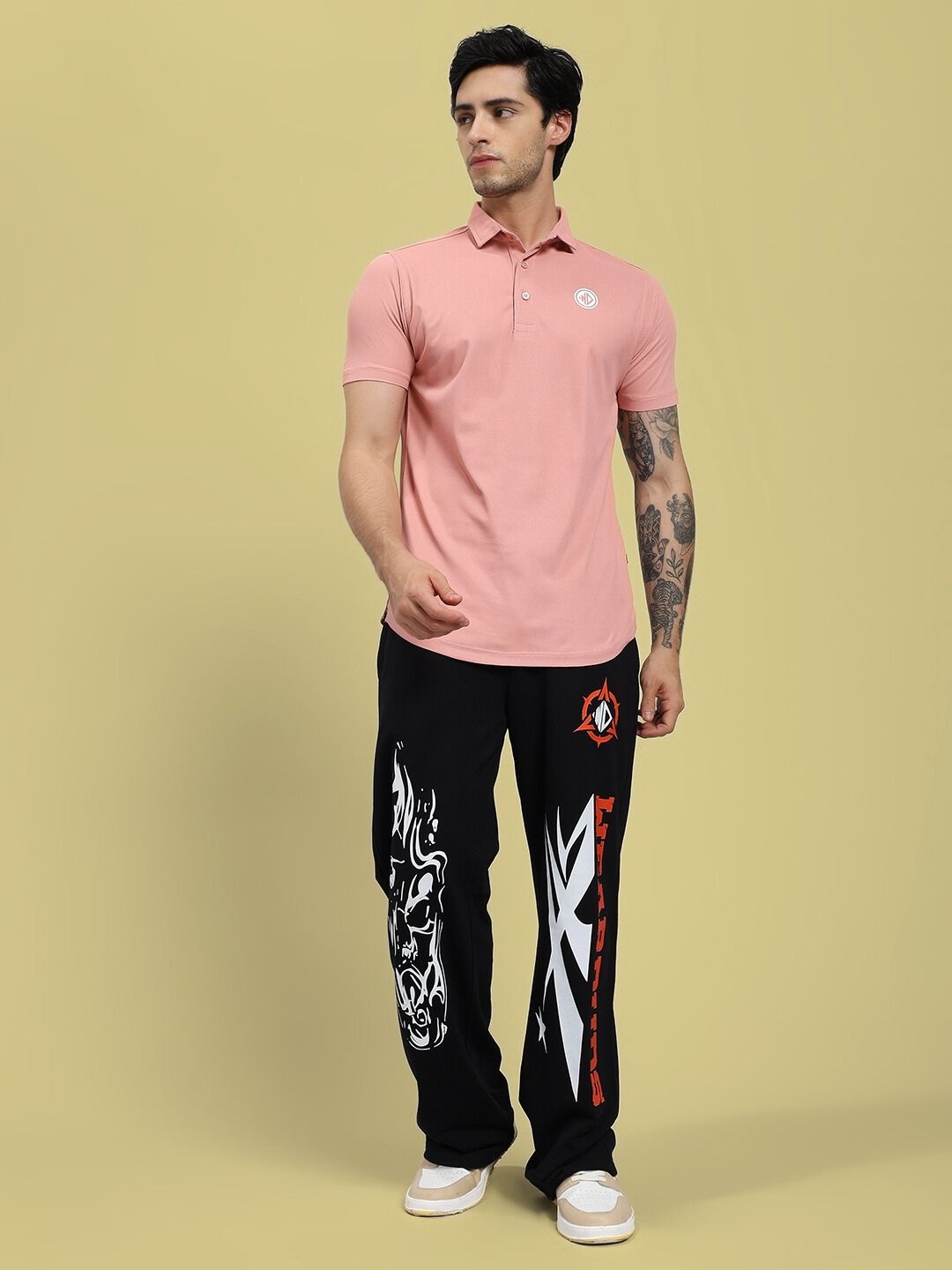 Man wearing a pink polo shirt and black pants with designs on a beige background