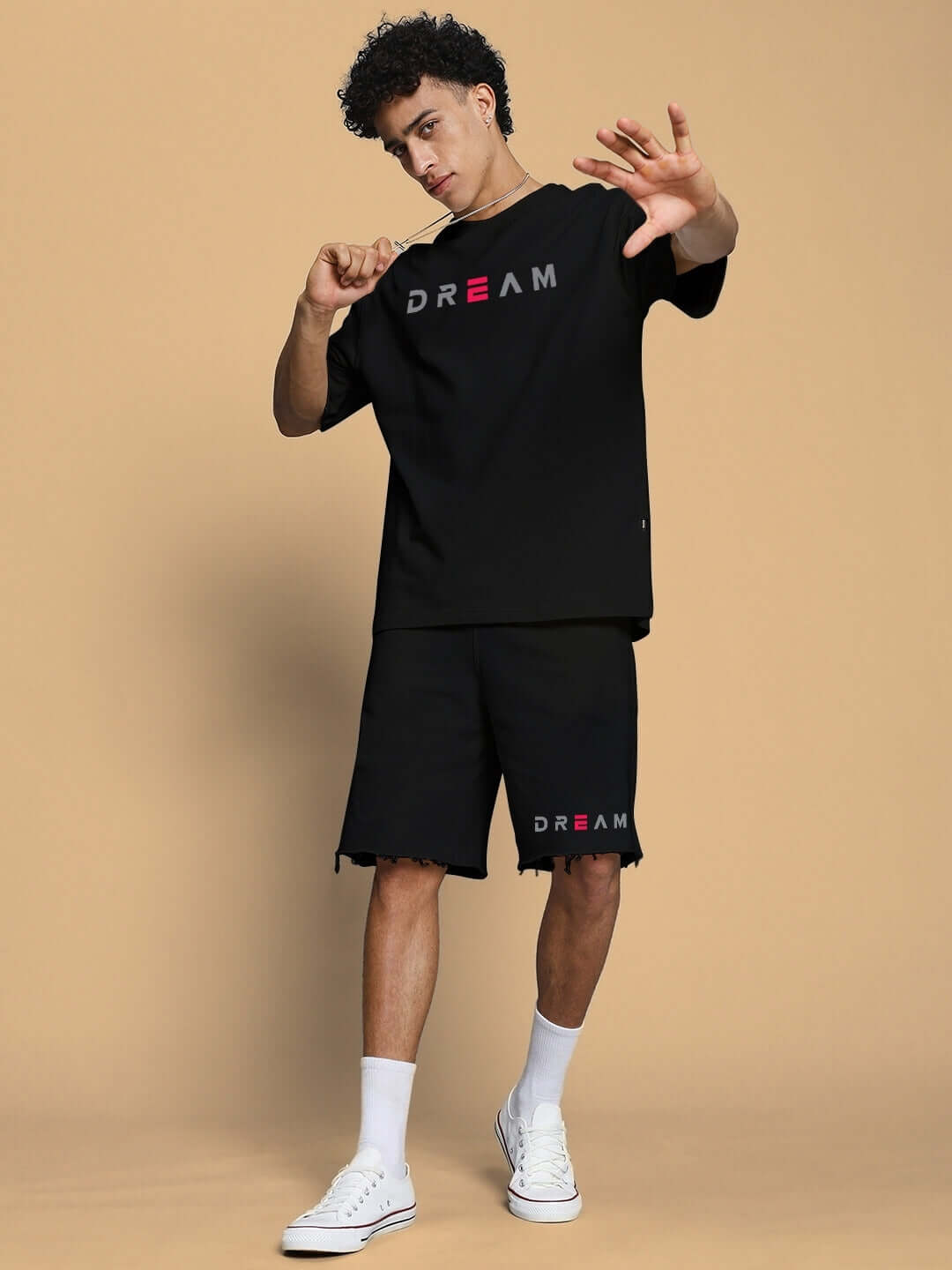 Model wearing black Fancy Dream regular fit shorts and matching T-shirt, posing with arms raised, on beige background.