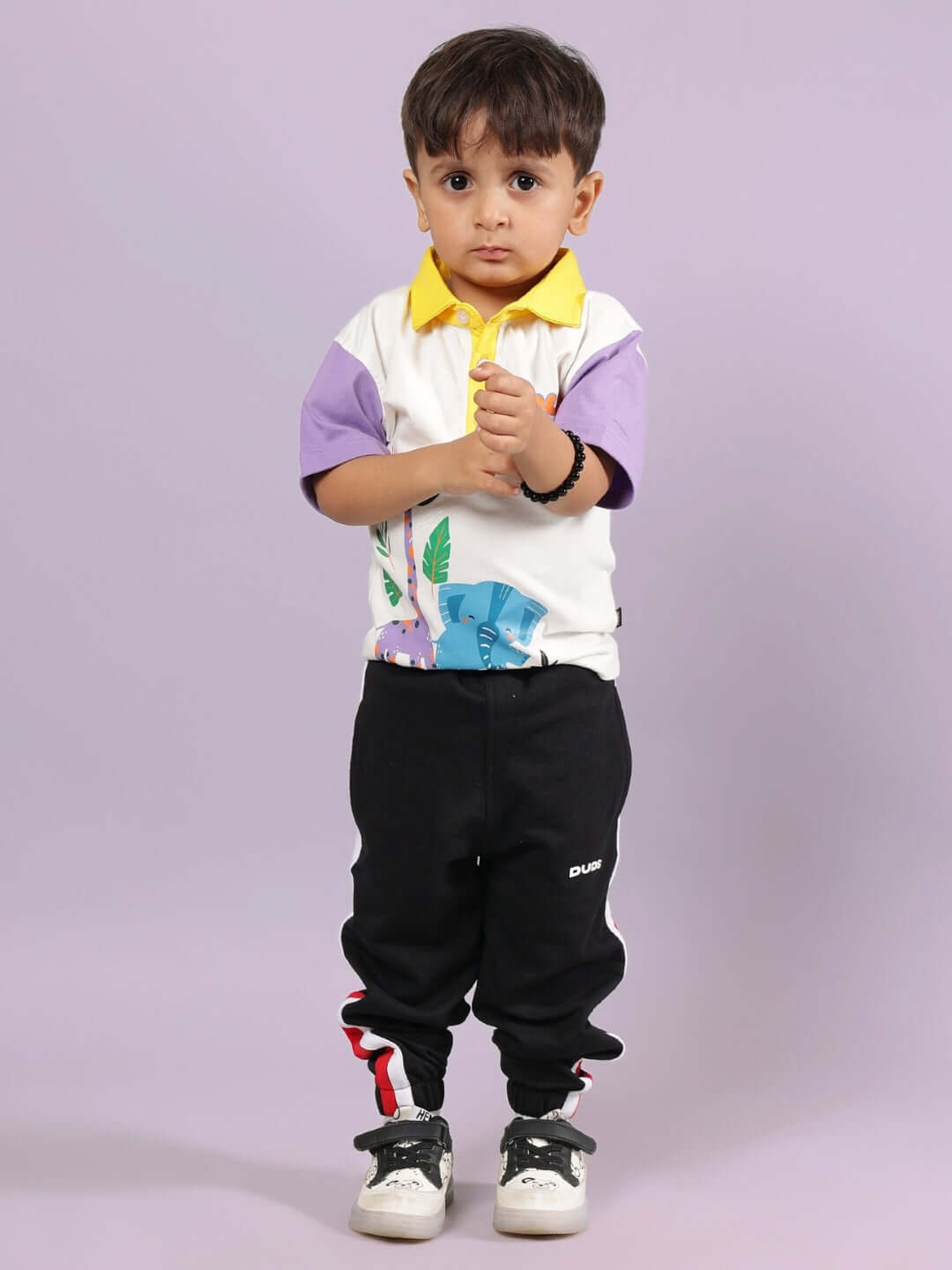 Young child wearing a colorful polo shirt and black pants, standing on a purple background.