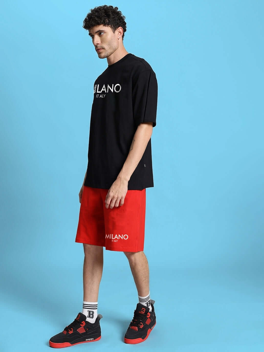Man wearing black and red ACRO summer co-ord set with Milano logo, showcasing sporty casual look against blue background.