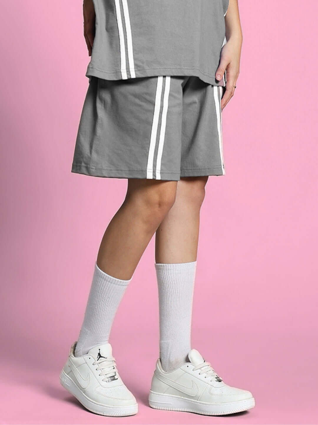 Women's grey shorts with white stripes, shown with white sneakers and socks on a pink background, ideal for casual wear.