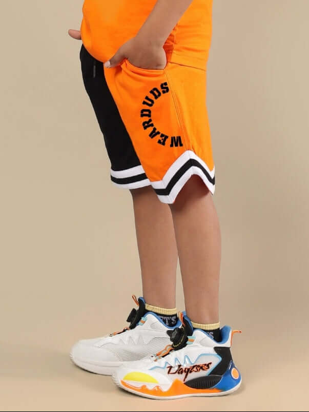 Child wearing black and orange track and field shorts by DUDS, customized size available, standing on beige background.