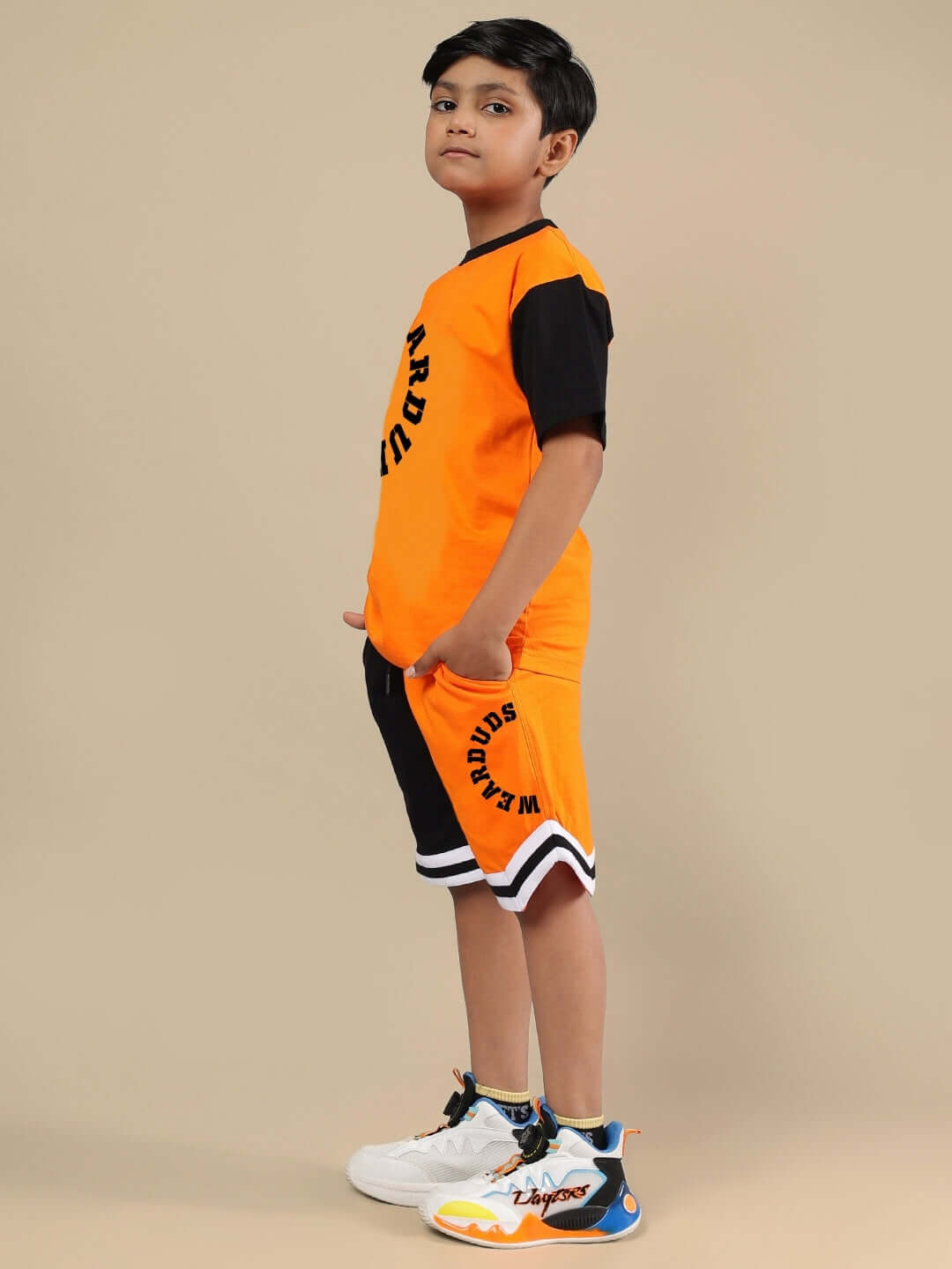 Orange and black track and field co-ord set for boys and girls, featuring sporty design, showcased by a young model standing sideways.