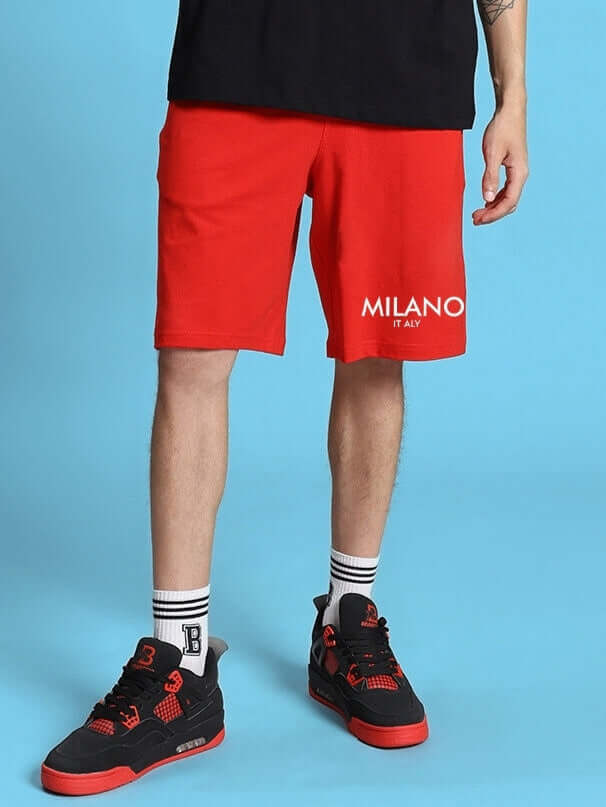 Man wearing red ACRO summer shorts and black sneakers on blue background.