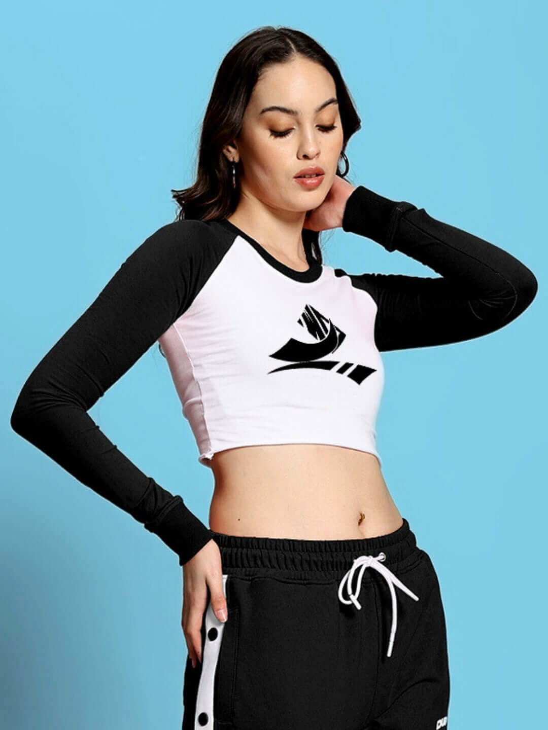 Woman wearing black and white long sleeve crop top with logo, paired with black drawstring pants, styled against a blue background.