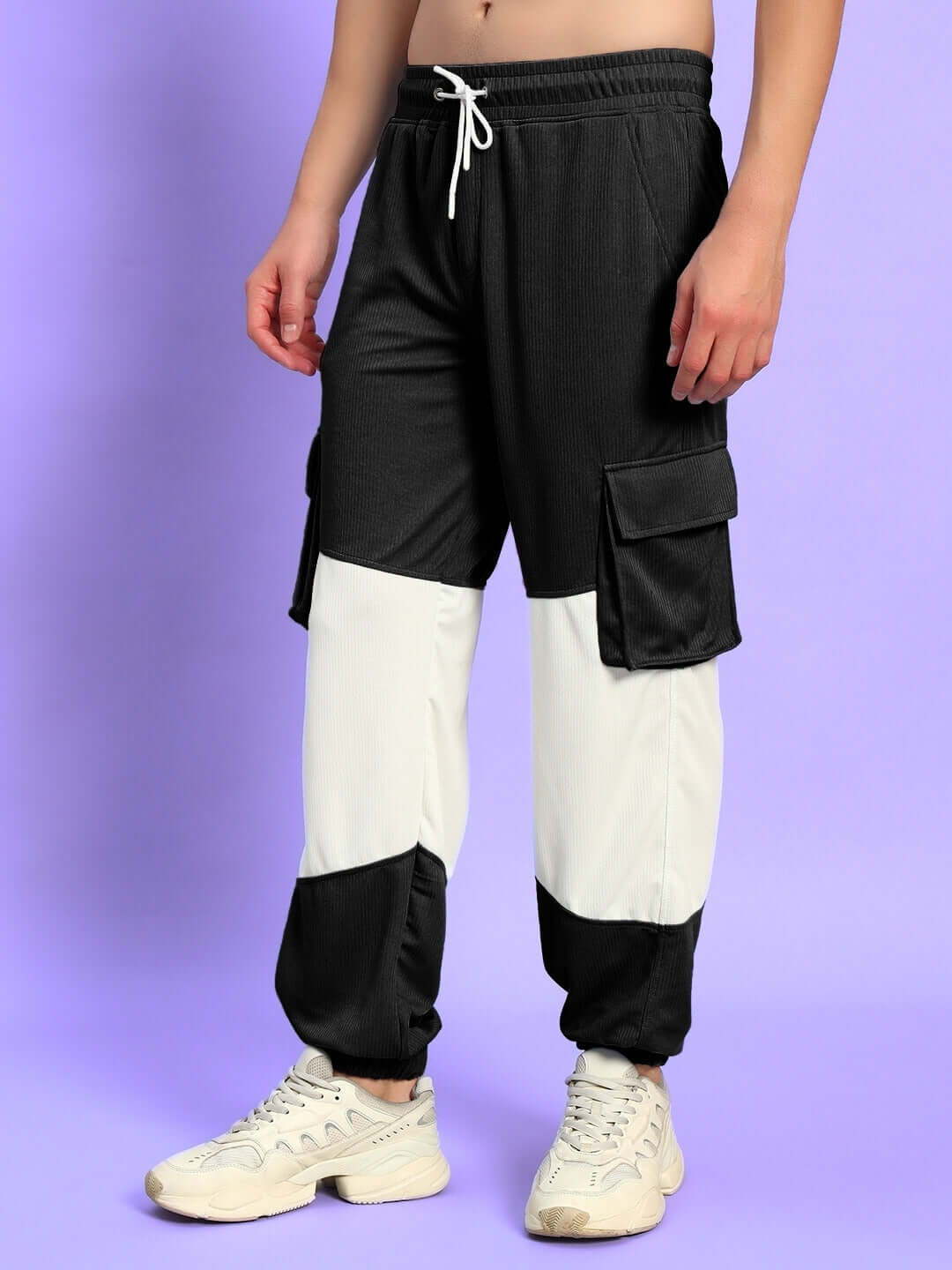 Model wearing black and white relaxed fit joggers with side pockets, showcasing comfortable and stylish design on a purple background.