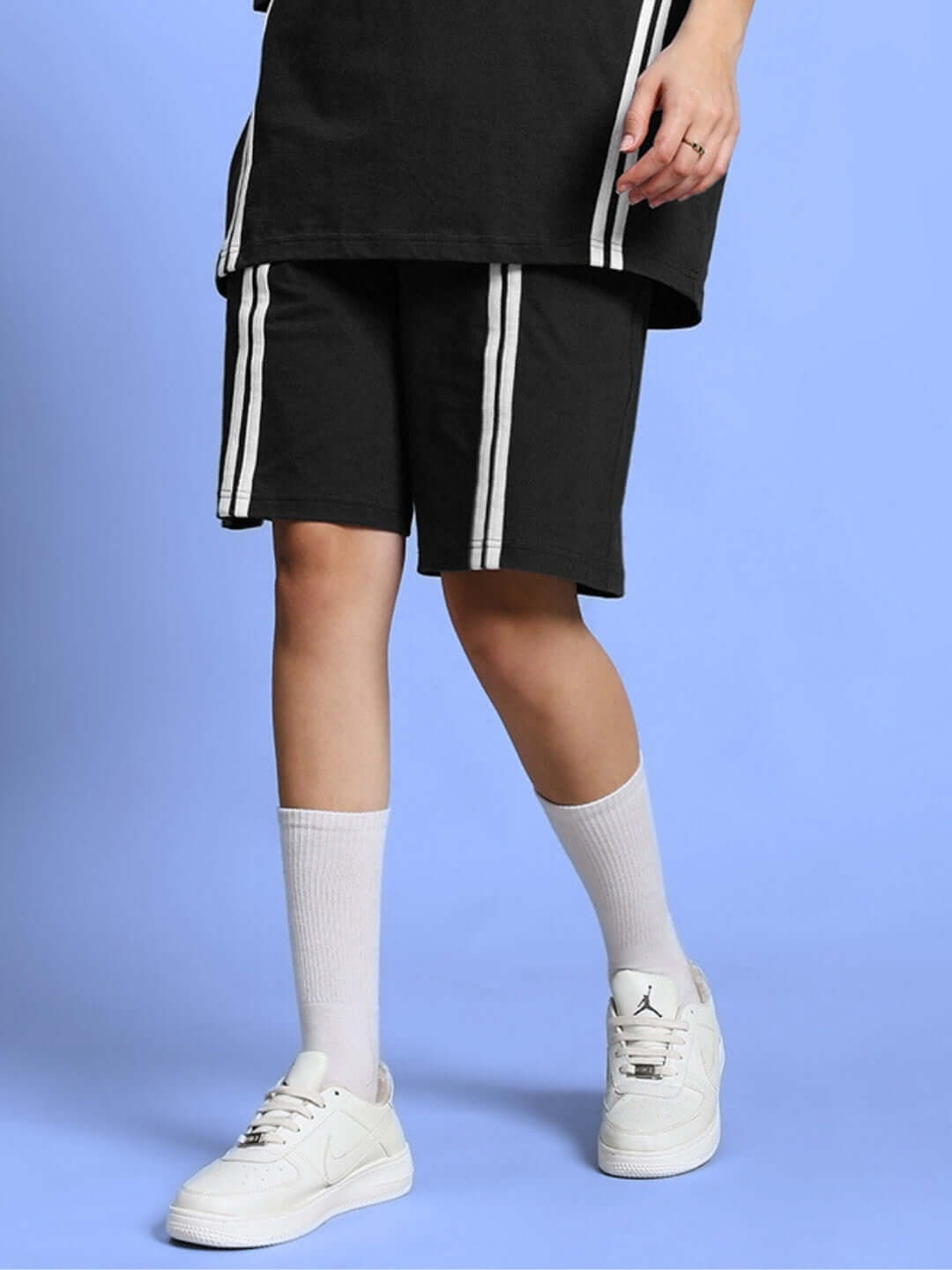 Woman wearing black regular fit shorts with white stripes, paired with white socks and sneakers, highlighting customizable fit options.