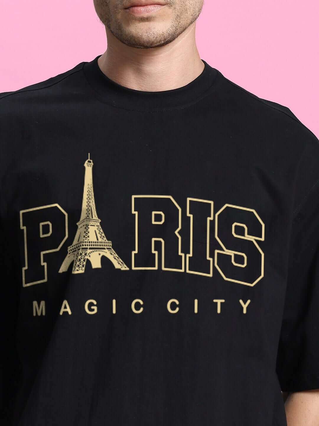 Close-up of a black t-shirt with 'PARIS MAGIC CITY' in gold, featuring an Eiffel Tower graphic on a pink background.