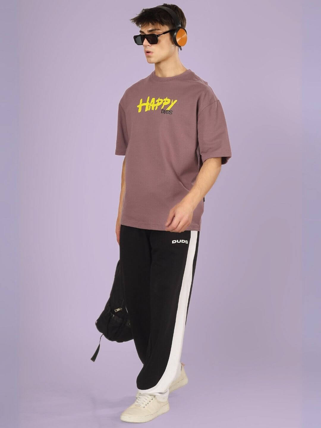 Model wearing HAPPY DUDS OVER-SIZED T-SHIRT CHINESE VOILET with black and white pants, headphones, and sunglasses.