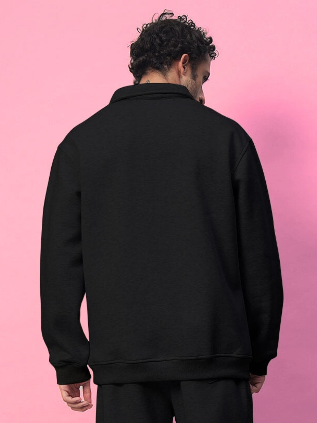Man wearing black Bona-Fide fleece sweatshirt, showcasing the back view against a pink background.
