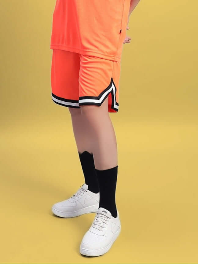 Model wearing Women's Chronic Regular Fit Shorts in orange with black and white trim, styled with white sneakers against a yellow background.