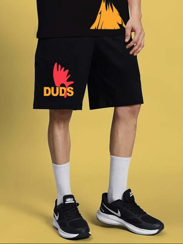 Black Funny Chicken summer shorts by DUDS with custom fit option displayed on a person wearing sneakers against a yellow background.