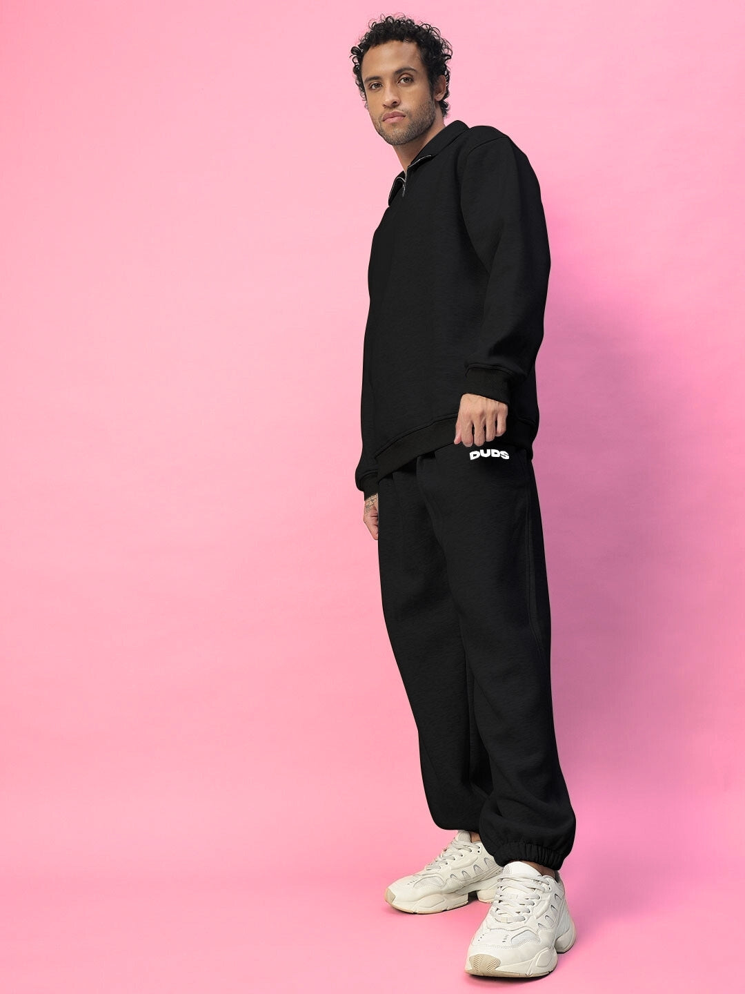 Model wearing black BONA-FIDE cotton fleece co-ord against a pink background, showcasing comfortable and stylish casual wear.