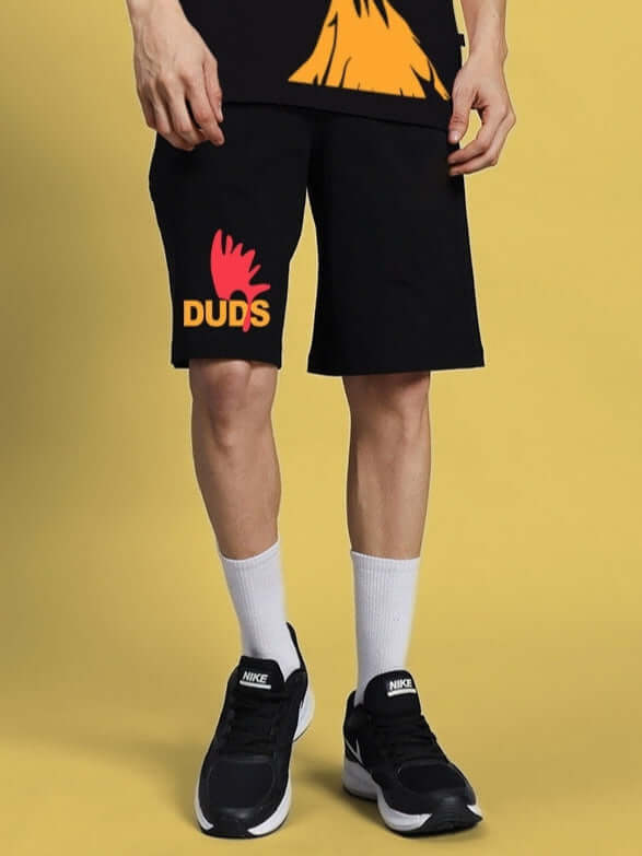 Person wearing black funny chicken summer shorts with DUDS logo, showcasing casual style against a yellow background.