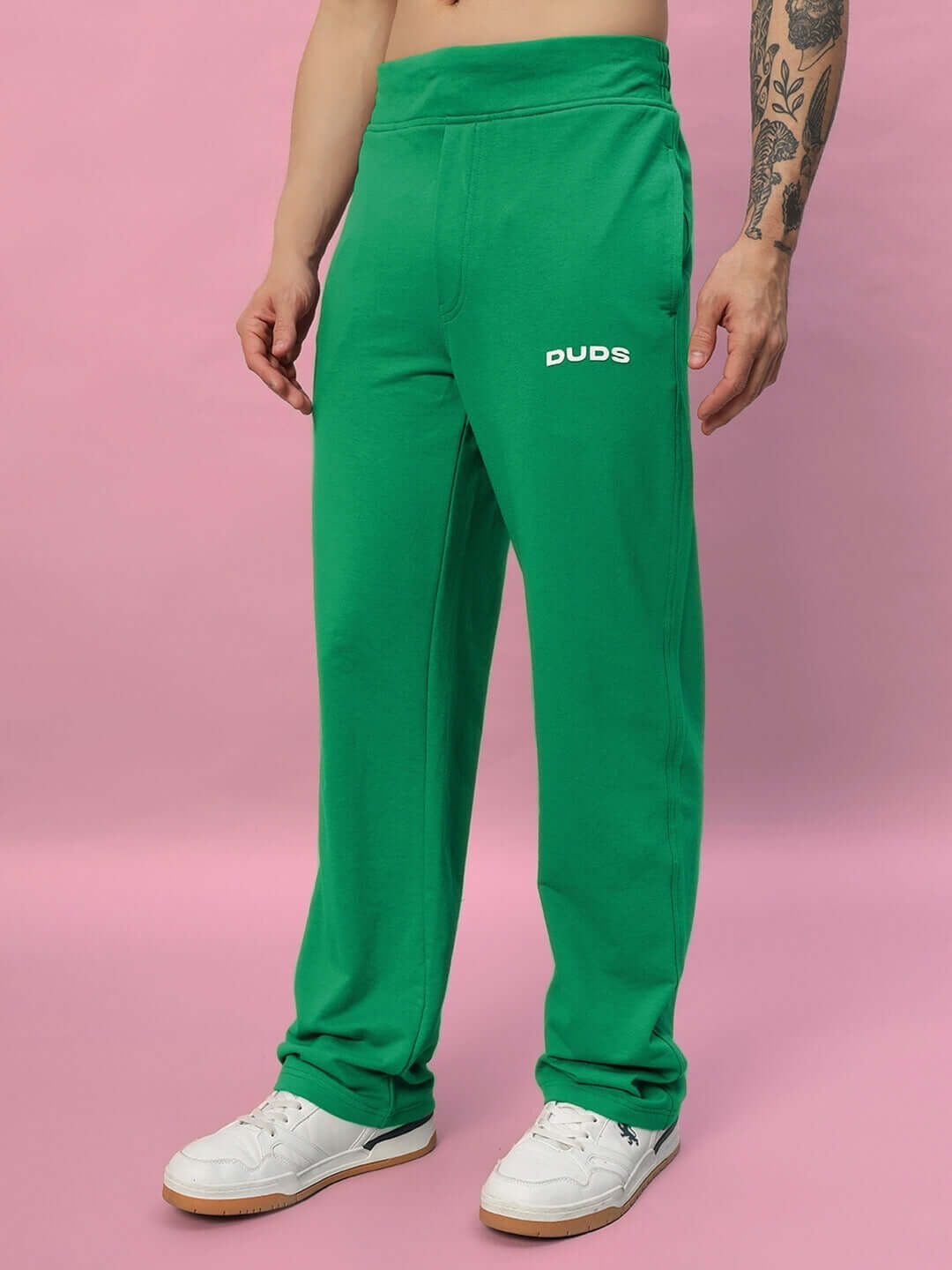 Model wearing green New Era Relaxed Fit Joggers by DUDS, showcasing casual style and comfort on a pink backdrop.