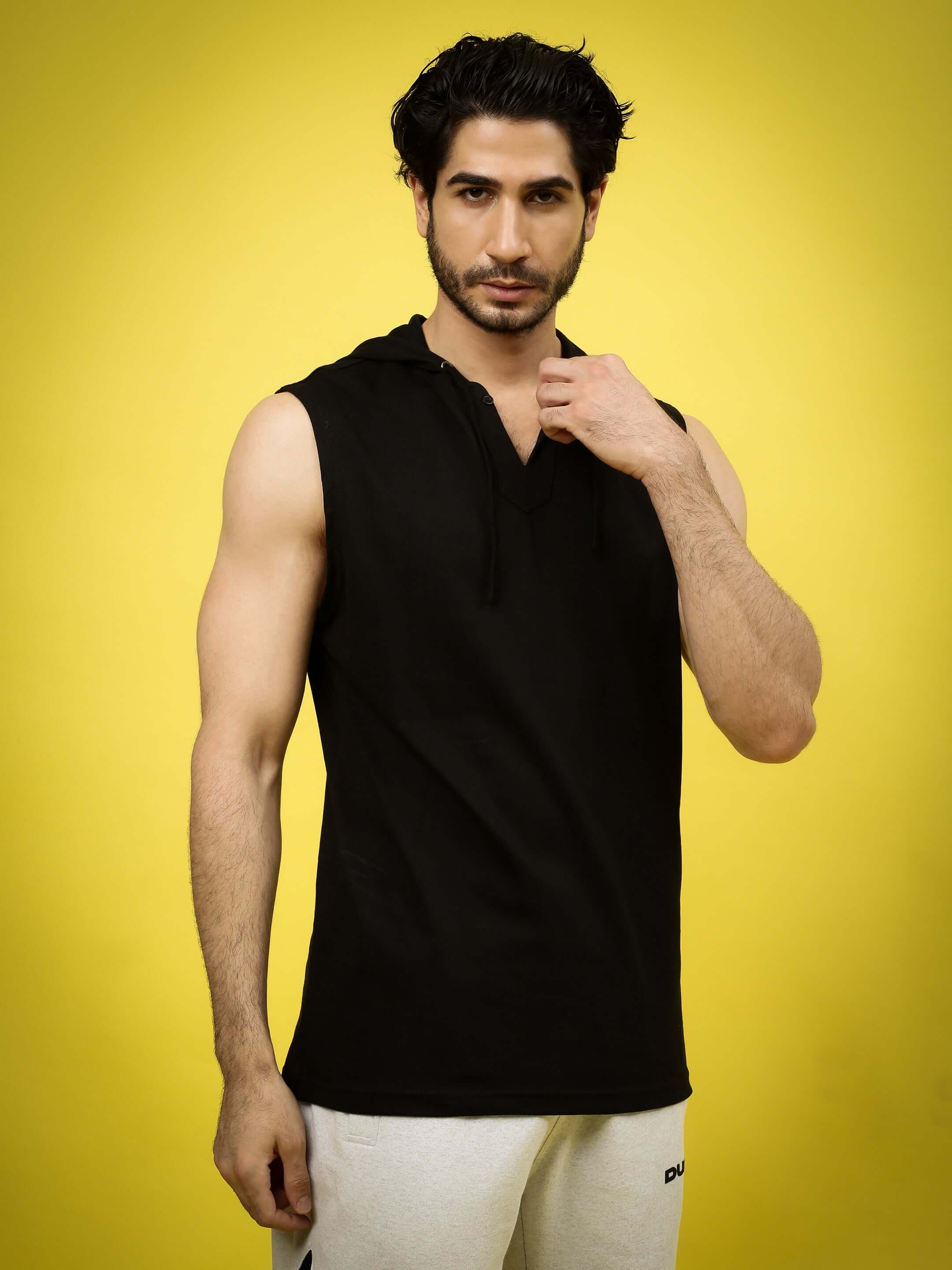 Model wearing ACME OVER-SIZED HOOD T-SHIRT BLACK, showcasing trendy streetwear style against a vibrant yellow background.