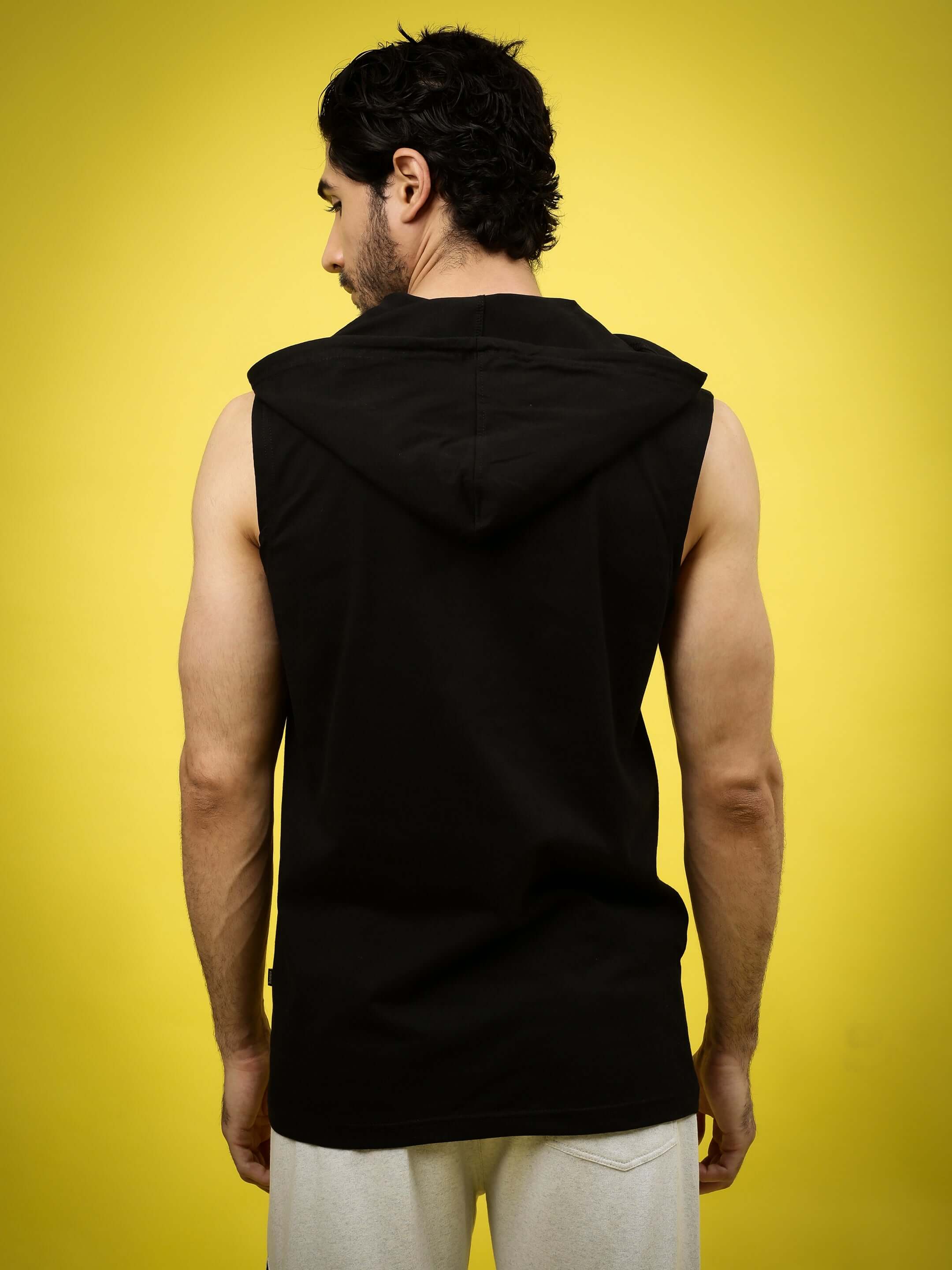 Back view of a model wearing the ACME OVER-SIZED HOOD T-SHIRT BLACK against a yellow background.