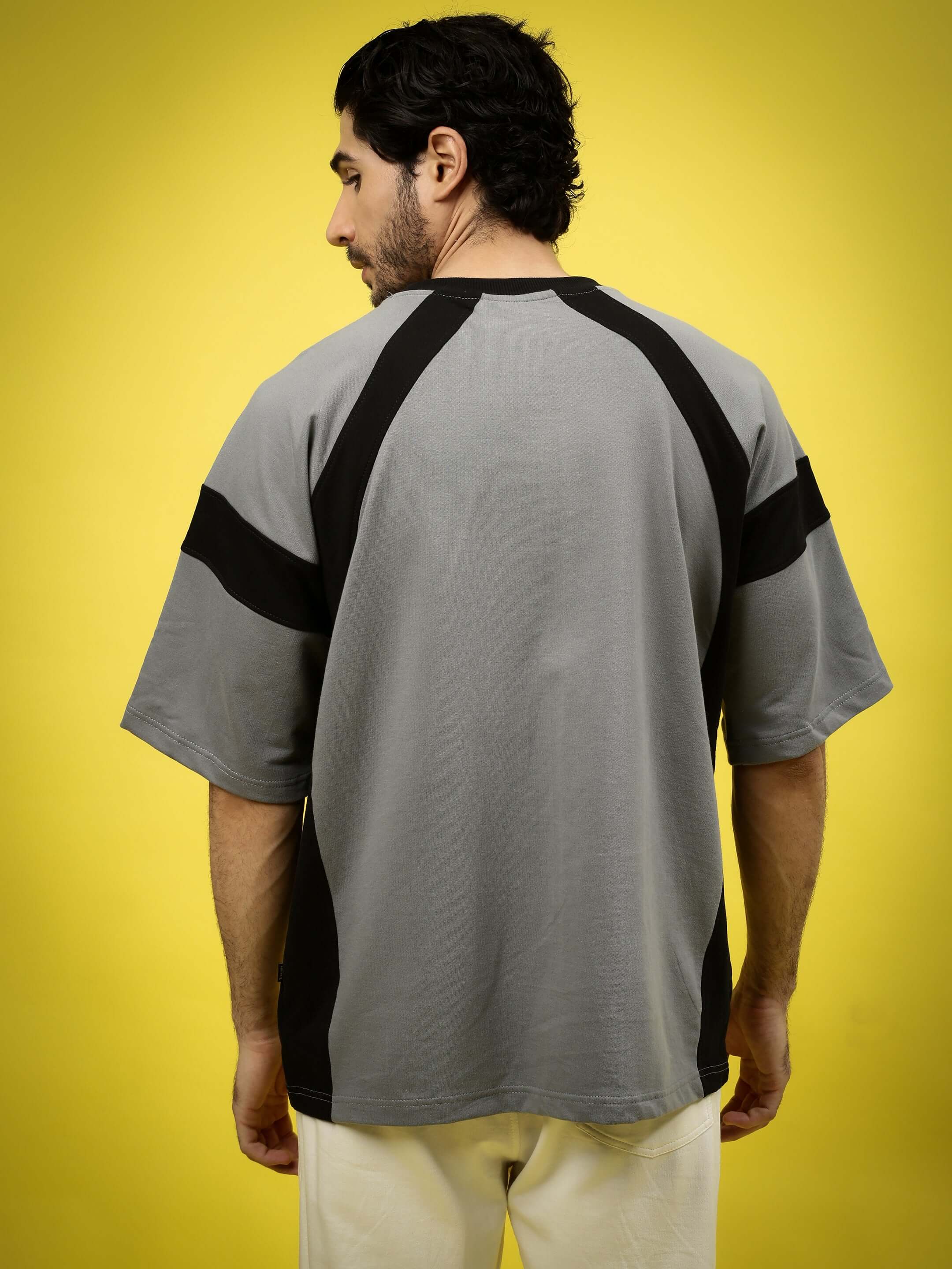 Model wearing a TURBO OVER-SIZED T-SHIRT SLATE GREY made of premium heavy gauge fabric with black accents on a yellow background.