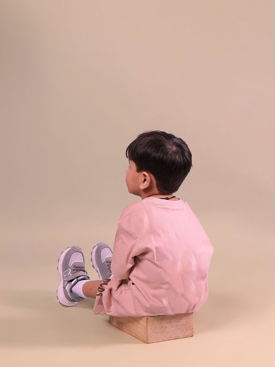 Child wearing the Flint Bunny co-ord set in beige, sitting on a wooden block against a soft background. Unisex outfit for boys and girls.