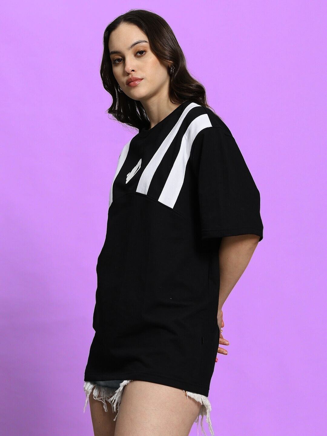 Woman wearing oversized black Allonzo t-shirt with white stripes, casual style, against purple background.