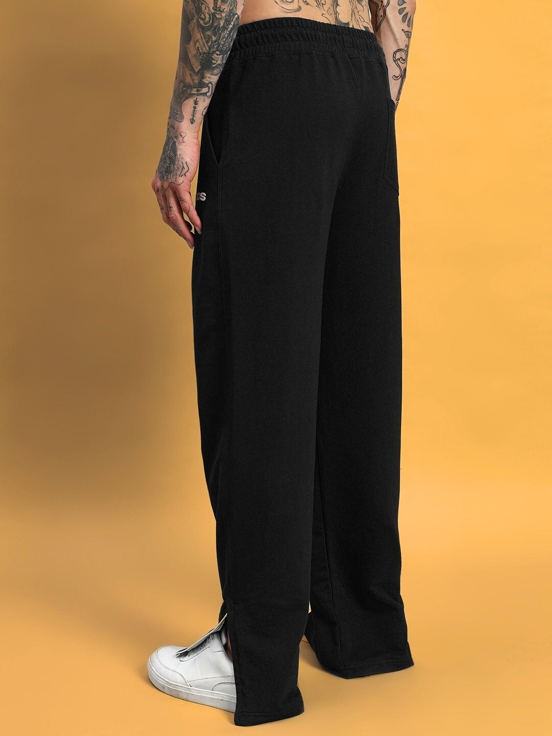 Back view of black HERSHEY side slit joggers worn by a model with tattoos, showcasing relaxed fit and white sneakers.