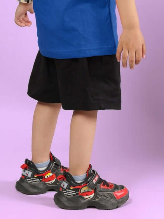 Young child wearing black Amiga shorts and colorful shoes against a pastel background.