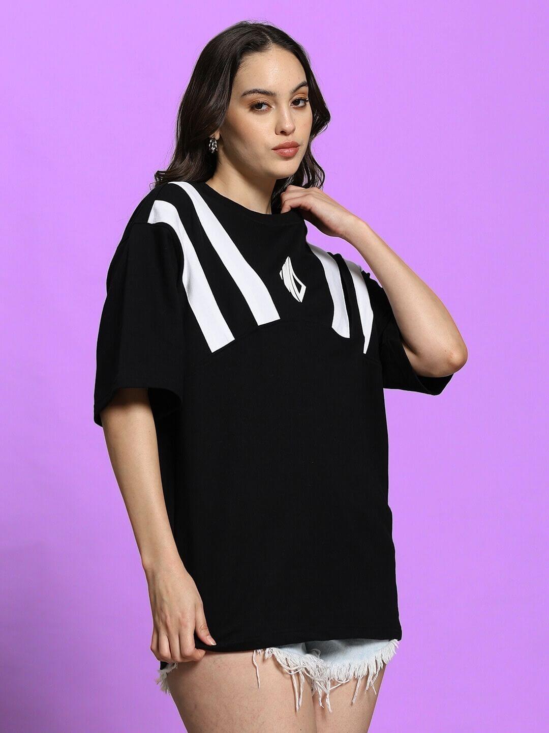 Woman wearing a black oversized Allonzo T-shirt with white stripe design, styled with denim shorts, against a purple background.