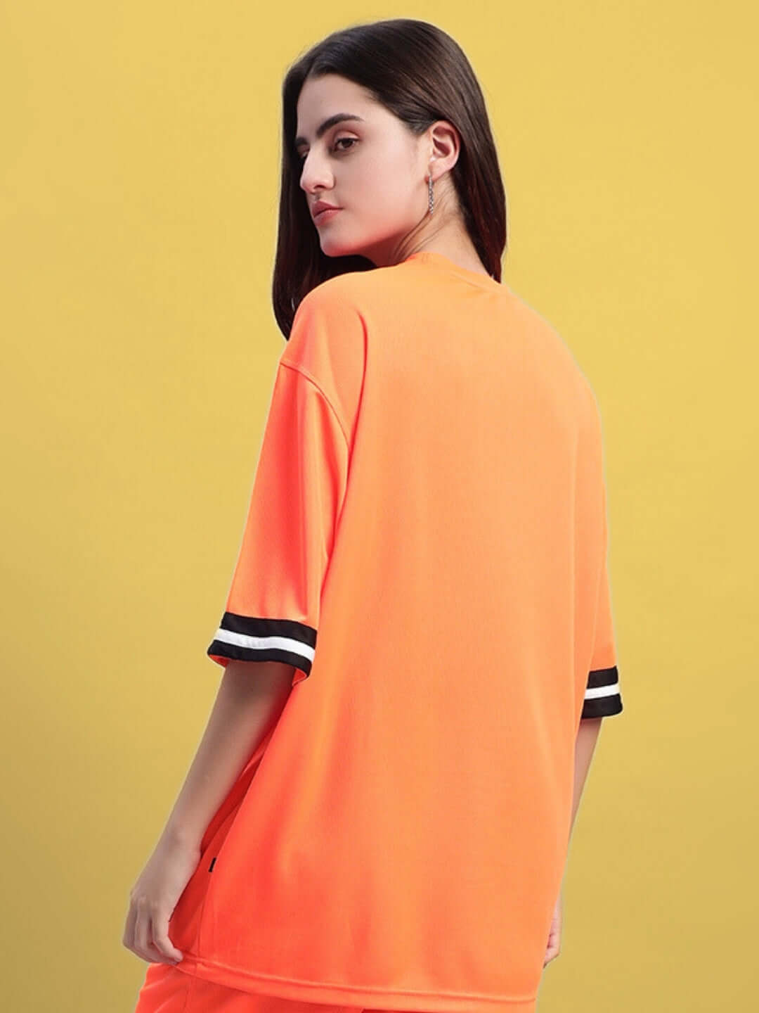 Woman wearing oversized orange t-shirt with striped sleeves on yellow background