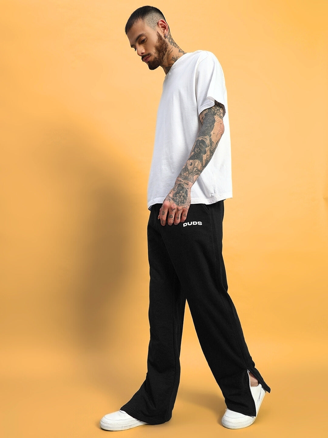 Model wearing black Hershey side slit joggers by DUDS, standing against a yellow background, showcasing comfortable streetwear style.