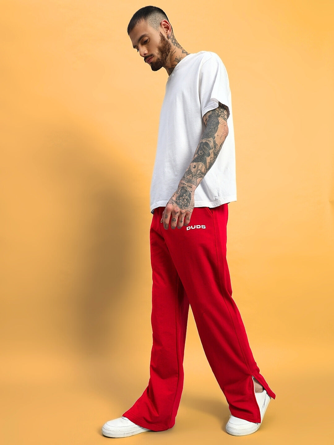 Model wearing red Hershey side slit joggers with DUDS logo, styled with a casual white t-shirt and sneakers on a solid background.