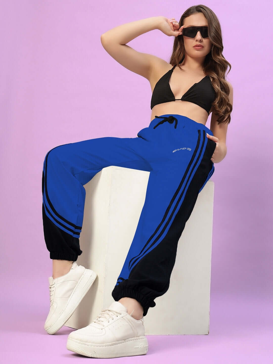 Model wearing Women's Frenzy Curve Contrast Joggers in blue and black, styled with white sneakers and sunglasses.