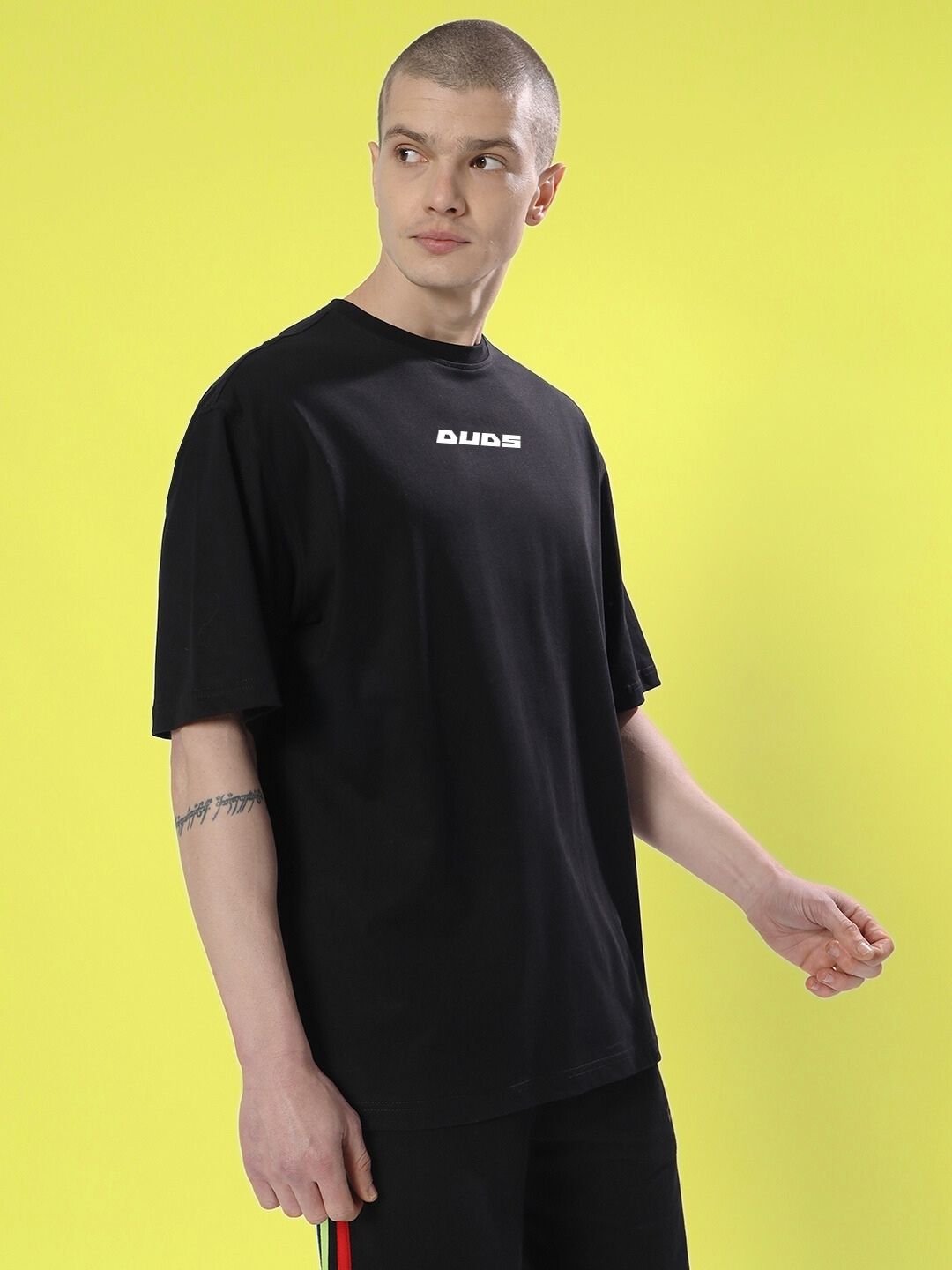 Person wearing a black SKULL CYBERPUNK OVERSIZED T-SHIRT BLACK with short sleeves, standing against a yellow background.